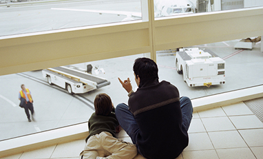 man and child sitting on ground pointing outside an airport window