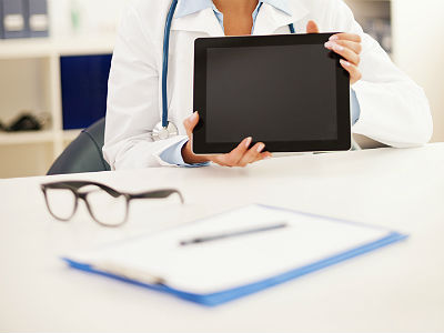 doctor holding up ipad with glasses and notepad on table